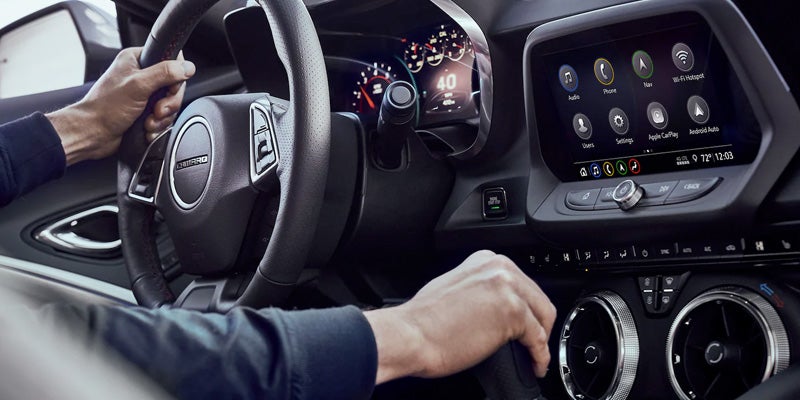 Multiple different functions options on the screen and a men is changing the gear while driving