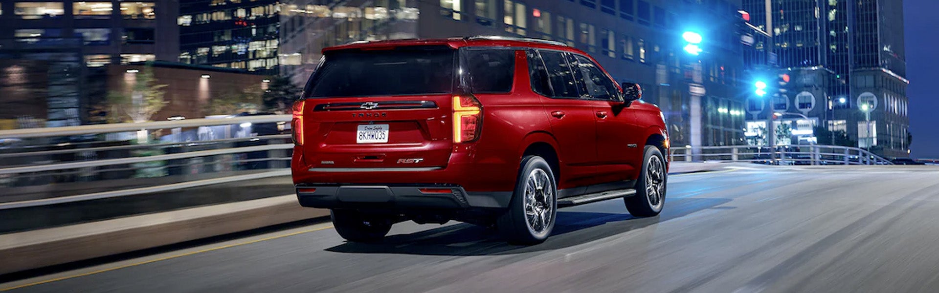 Red Chevrolet Tahoe running on a road at night rear view