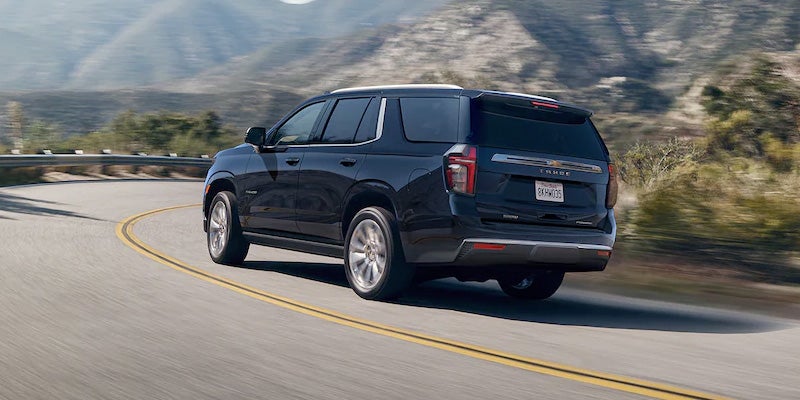 Black Chevrolet Tahoe running on road between hills