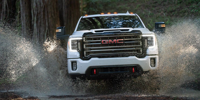 GMC Sierra HD truck off-road, splashing water, rugged terrain.