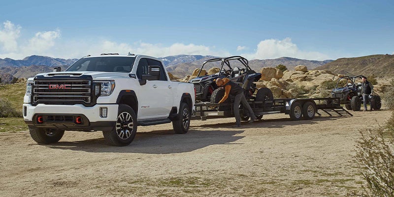 GMC Sierra HD towing trailer with off-road vehicles in desert