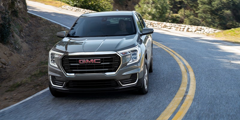 Grey GMC Terrain running on road between hills